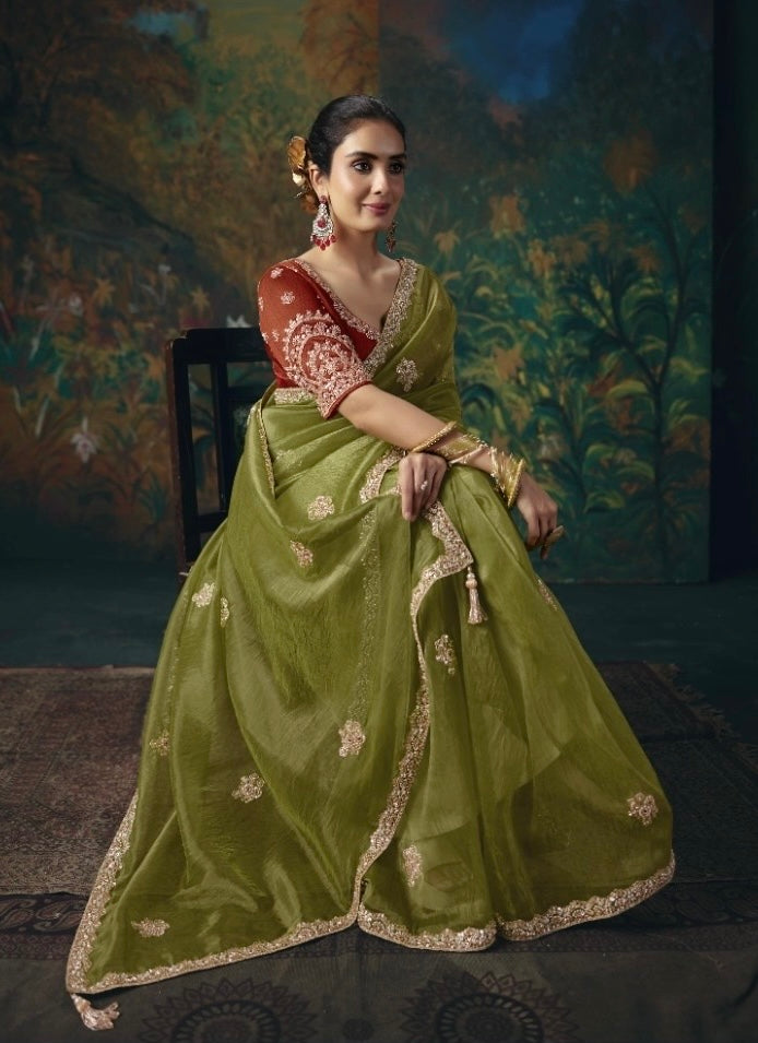 Olive green tissue silk saree draped while seated, with gold floral accents and ornate border