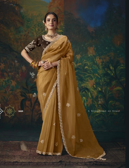Mustard-gold tissue silk saree with ornate embroidered border and scattered floral motifs, worn with a dark blouse
