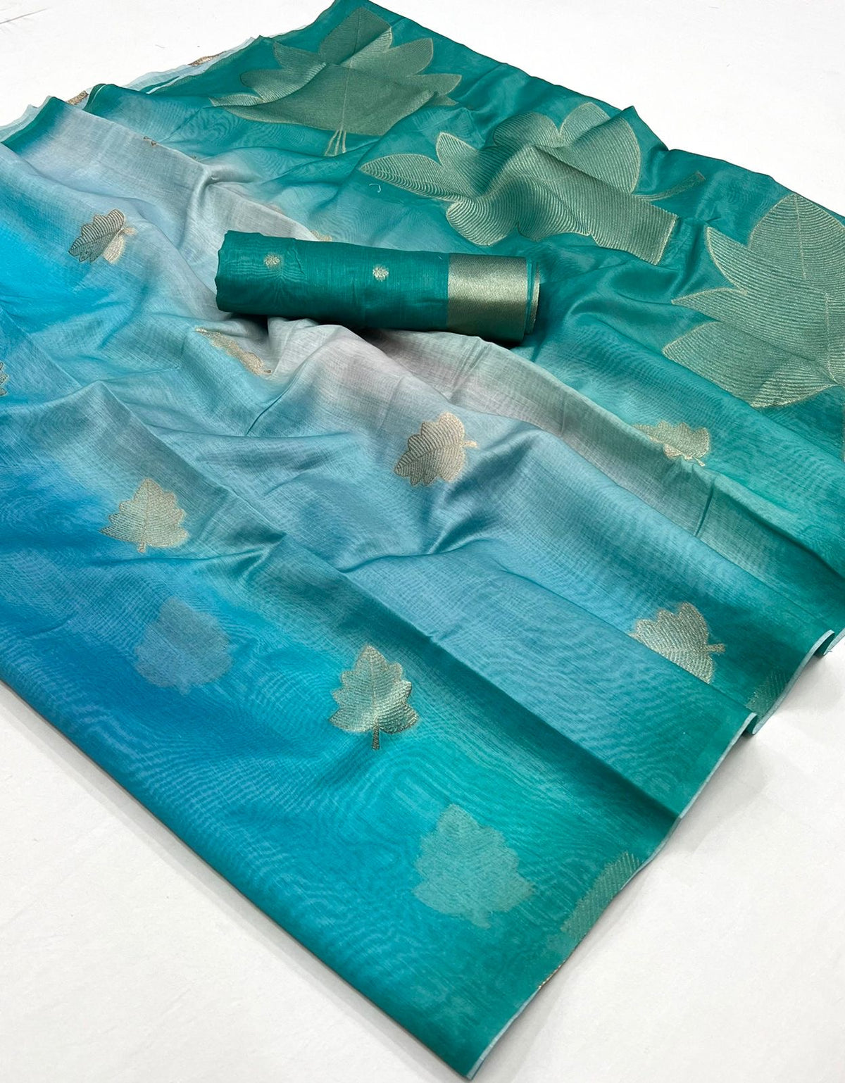 Folded turquoise and teal printed linen saree with gold motifs and contrast green border