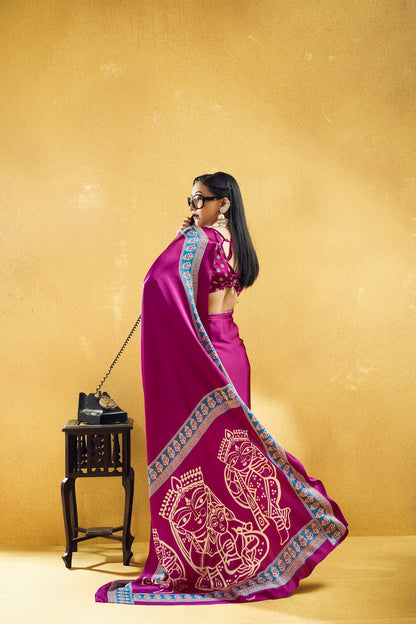 A woman wearing a bright magenta-purple traditional Indian outfit with a patterned dupatta and sunglasses, standing in profile against a textured gold background next to a small black table holding a black clutch.